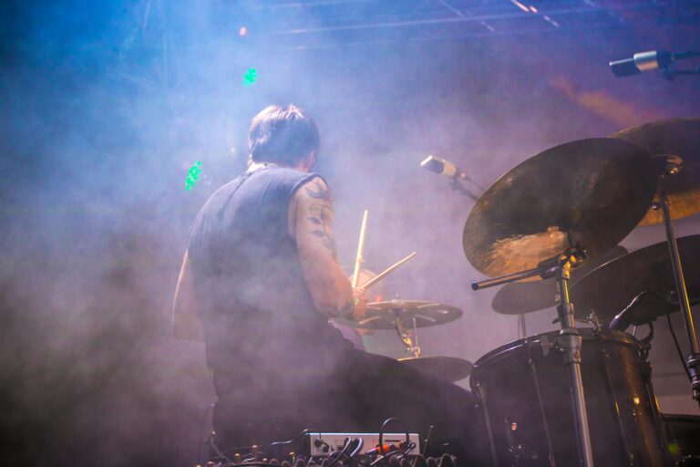 Energetic drummer performing live on stage with colorful smoke and lighting effects.